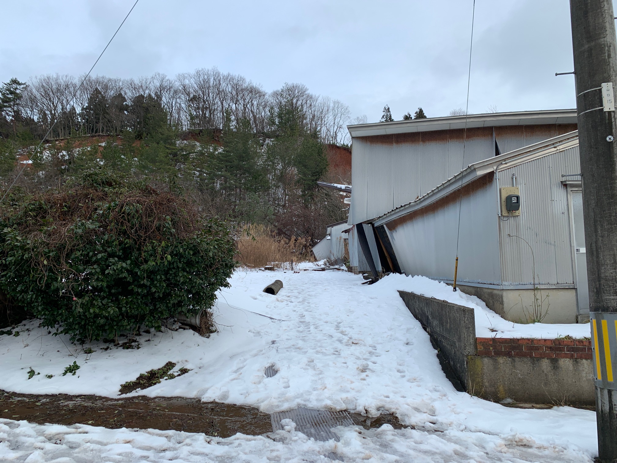 雪の残る庭と、傾いた塀のある住宅